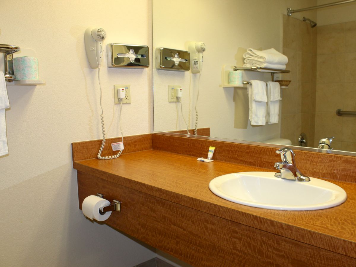 The image shows a bathroom with a countertop, a sink, a wall-mounted hairdryer, towels, and a mirror above the counter.