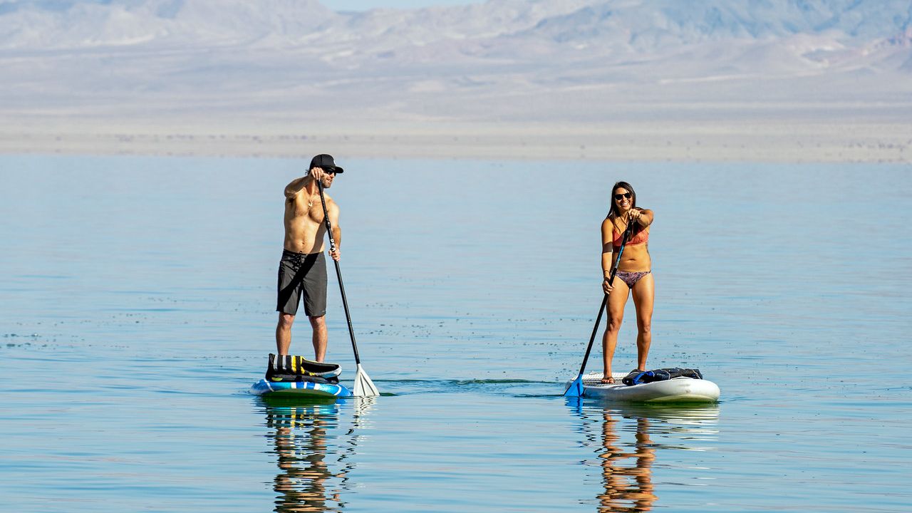 Two people paddleboarding on a calm body of water, with mountains in the background.