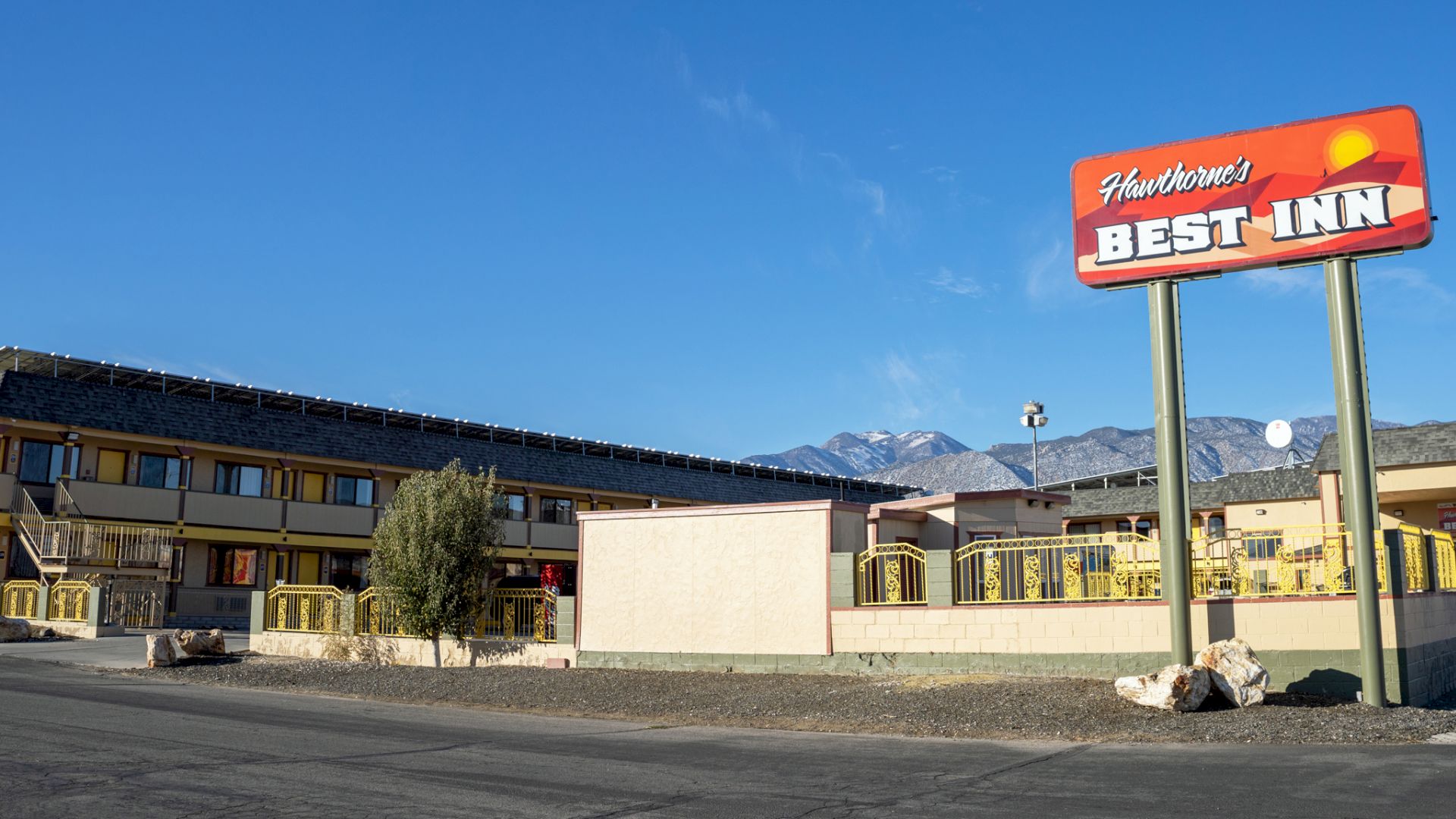 The image shows a building with a sign that reads "Hawthorne's BEST INN" on a tall pole, against a backdrop of mountains and a clear sky.