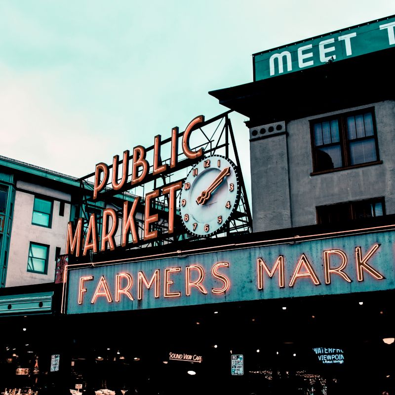 This image shows the neon signs for "Public Market" and "Farmers Market" at Pike Place Market in Seattle, a well-known historic market and landmark.