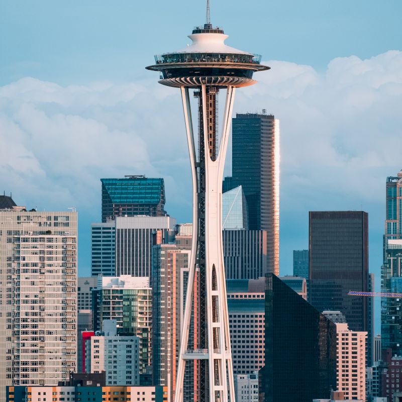 The image features the Seattle Space Needle with a backdrop of various high-rise buildings and a partly cloudy sky in the background.