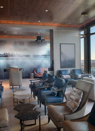 A cozy lounge area with rows of comfortable seating, large windows with a scenic view, and a mural of a cityscape on the wall.