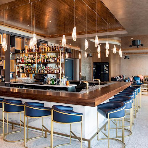 The image shows a modern bar with stylish seating, pendant lights, and a fully stocked liquor shelf behind the counter ending the sentence.