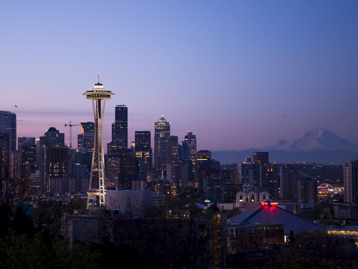 The image shows the Seattle skyline with the Space Needle prominently lit against a twilight sky and Mount Rainier in the background.
